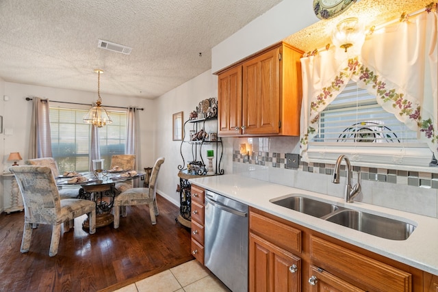 kitchen with light countertops, backsplash, brown cabinetry, a sink, and dishwasher