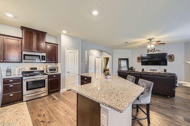 kitchen with arched walkways, light wood-style flooring, a center island, and stainless steel appliances