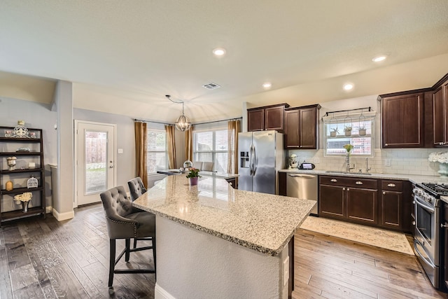 kitchen featuring a breakfast bar area, stainless steel appliances, wood-type flooring, and a sink