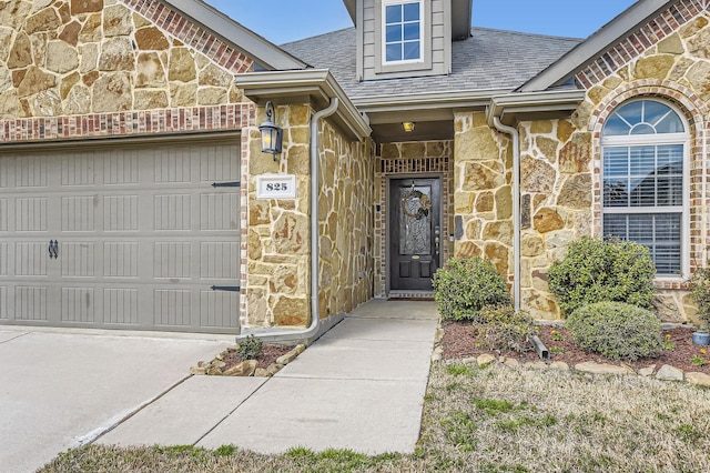 entrance to property with stone siding, an attached garage, driveway, and roof with shingles