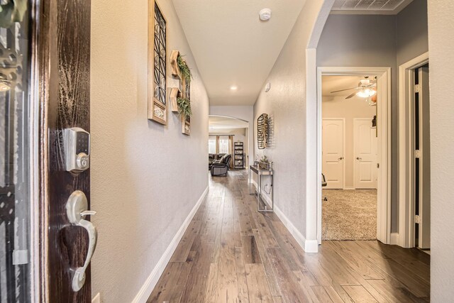 hallway featuring baseboards, arched walkways, hardwood / wood-style floors, and a textured wall