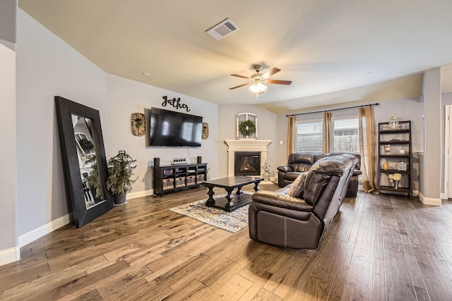 living room featuring a glass covered fireplace, visible vents, wood-type flooring, and ceiling fan