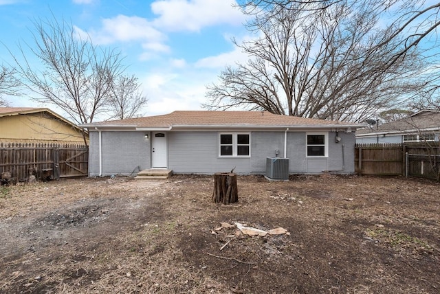 rear view of house with entry steps, a fenced backyard, central AC unit, and brick siding