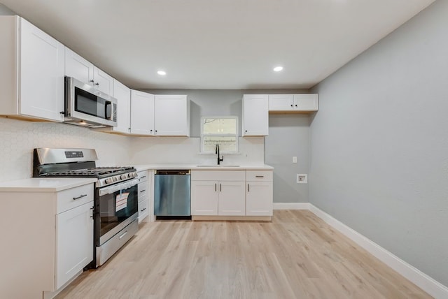 kitchen featuring appliances with stainless steel finishes, light wood-style floors, white cabinets, a sink, and baseboards