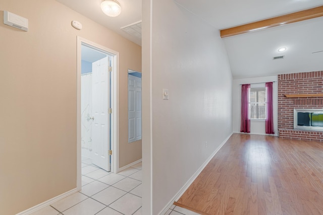 interior space featuring vaulted ceiling with beams, visible vents, light wood-style floors, baseboards, and a brick fireplace