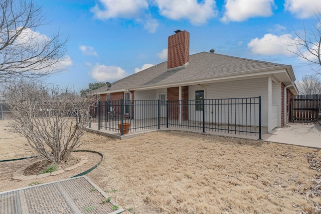 back of property with brick siding, roof with shingles, a chimney, a patio area, and fence