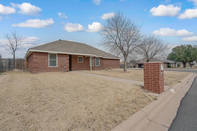 view of front facade with brick siding, fence, and roof with shingles