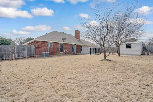 back of house with an outbuilding, central AC unit, a fenced backyard, brick siding, and a chimney