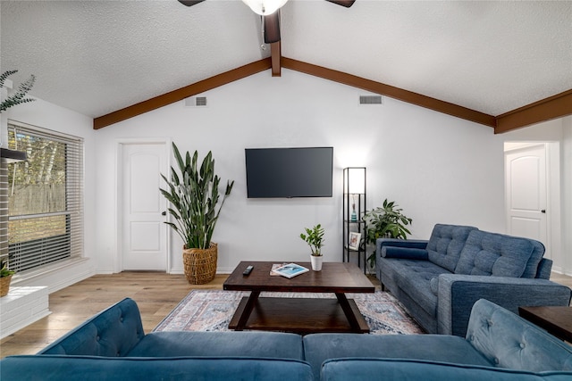 living area featuring visible vents, a ceiling fan, a textured ceiling, wood finished floors, and vaulted ceiling with beams