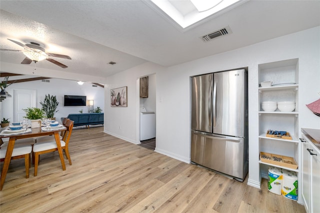 kitchen with light wood finished floors, visible vents, a skylight, freestanding refrigerator, and washer / clothes dryer