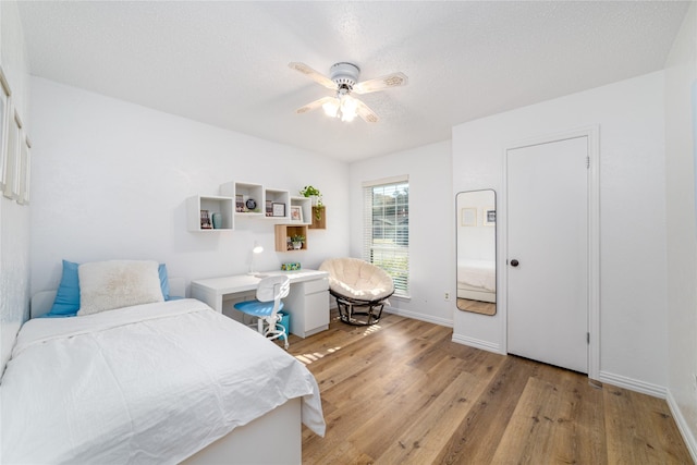 bedroom featuring a textured ceiling, baseboards, light wood finished floors, and ceiling fan