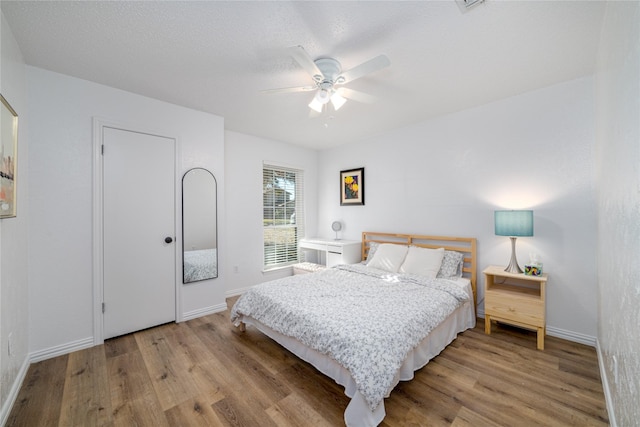 bedroom featuring light wood finished floors, ceiling fan, a textured ceiling, and baseboards