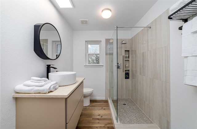 bathroom featuring visible vents, toilet, wood finished floors, and a tile shower