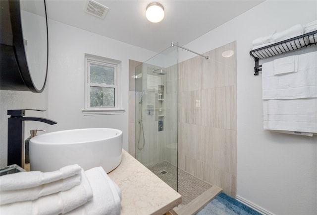 full bath with a sink, visible vents, baseboards, and a tile shower