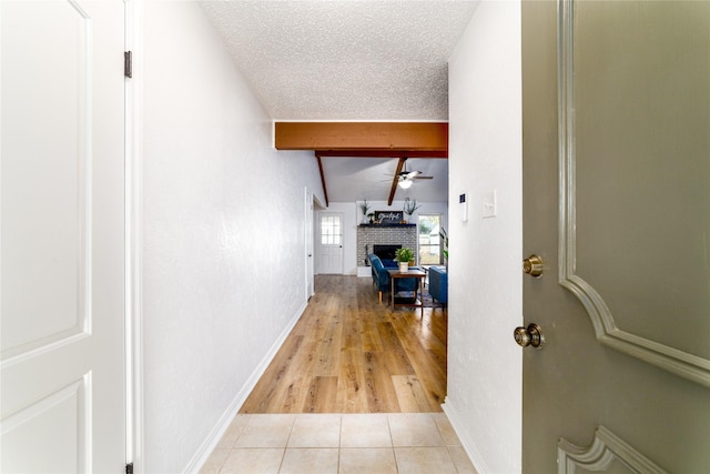 hall with light tile patterned floors, vaulted ceiling with beams, a textured ceiling, and baseboards