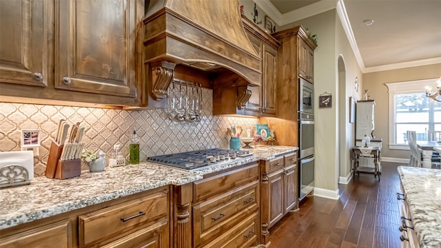 kitchen featuring arched walkways, light stone counters, ornamental molding, dark wood-type flooring, and premium range hood