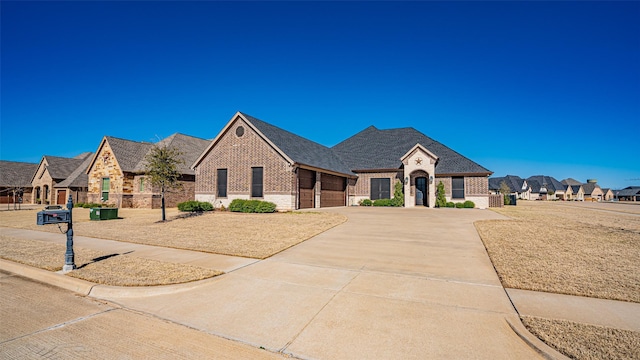 french provincial home with a garage, concrete driveway, a residential view, roof with shingles, and brick siding