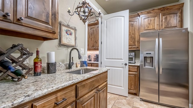 kitchen featuring stainless steel refrigerator with ice dispenser, stone finish floor, a sink, light stone countertops, and a chandelier