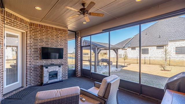 unfurnished sunroom featuring wood ceiling, an outdoor fireplace, and a ceiling fan