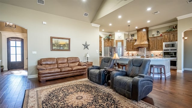 living area with arched walkways, dark wood finished floors, and ornamental molding