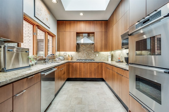 kitchen with stainless steel appliances, backsplash, a sink, light stone countertops, and wall chimney exhaust hood