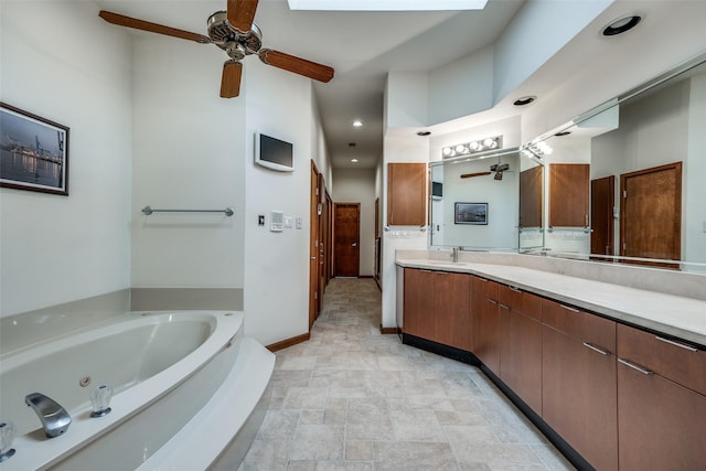 full bathroom with a skylight, vanity, baseboards, a whirlpool tub, and stone finish flooring