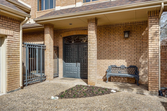 doorway to property featuring a shingled roof and brick siding