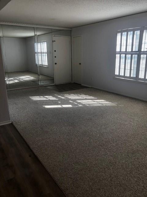 spare room with dark carpet, a textured ceiling, and baseboards