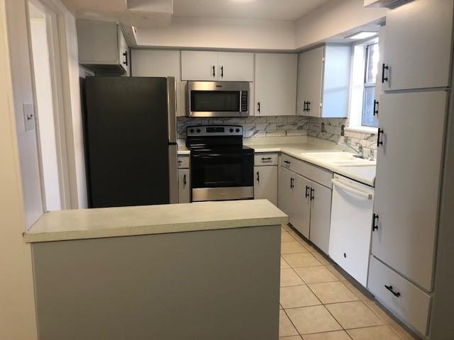 kitchen featuring light tile patterned floors, decorative backsplash, appliances with stainless steel finishes, a sink, and a peninsula