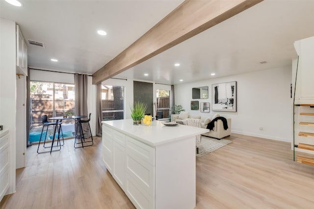 kitchen with white cabinets, visible vents, beamed ceiling, and light wood-style flooring