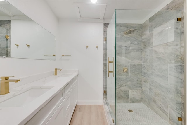 full bath with wood finished floors, a sink, baseboards, a shower stall, and double vanity