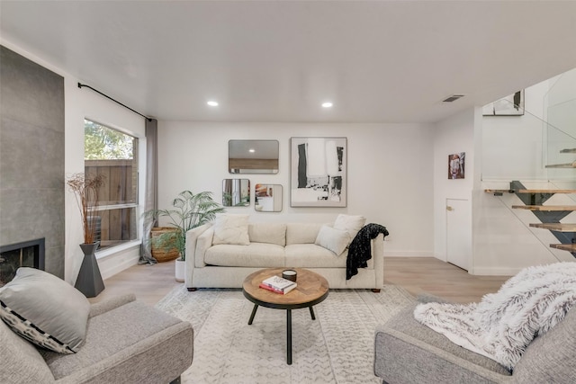 living room featuring visible vents, light wood finished floors, a tiled fireplace, and stairs