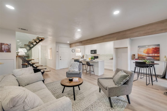 living room featuring recessed lighting, visible vents, light wood-style flooring, and stairs