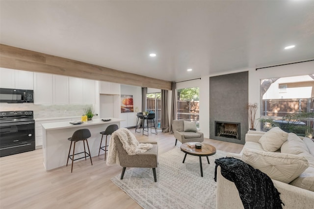 living area with light wood finished floors, a large fireplace, and recessed lighting