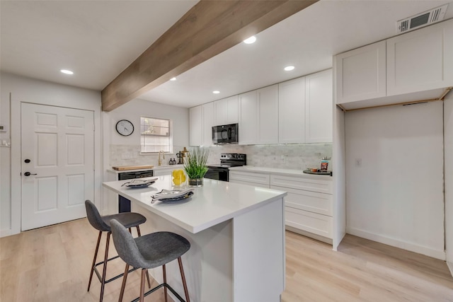 kitchen with a breakfast bar, visible vents, white cabinets, black appliances, and light wood finished floors