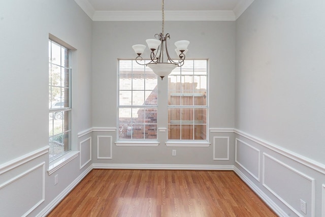 unfurnished dining area featuring a chandelier, light wood-type flooring, a decorative wall, and ornamental molding