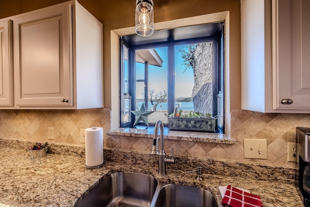 kitchen with a sink, light stone counters, tasteful backsplash, and white cabinetry