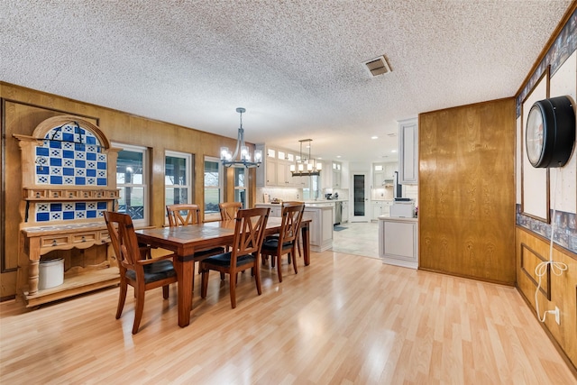 dining space with visible vents, wood walls, light wood-style floors, and an inviting chandelier