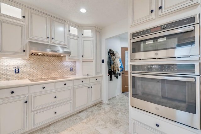 kitchen with backsplash, black electric stovetop, under cabinet range hood, double oven, and light countertops