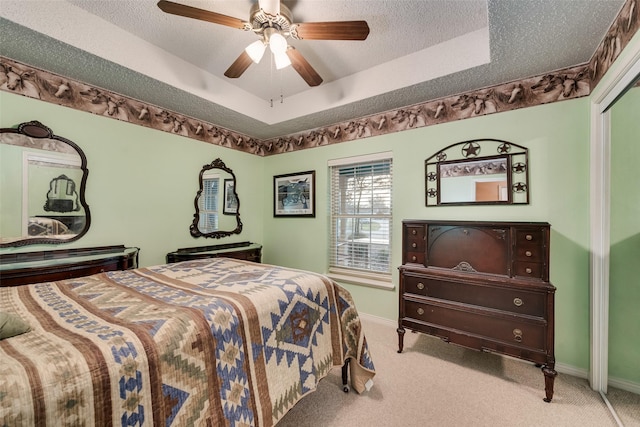 bedroom featuring a textured ceiling, a tray ceiling, baseboards, and light carpet