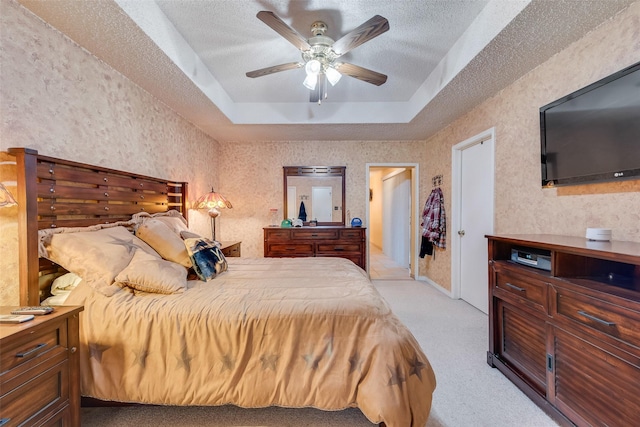 bedroom with a tray ceiling, light carpet, a textured ceiling, and a ceiling fan