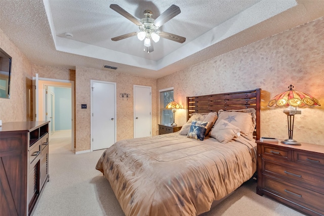 bedroom with visible vents, wallpapered walls, light carpet, a textured ceiling, and a raised ceiling