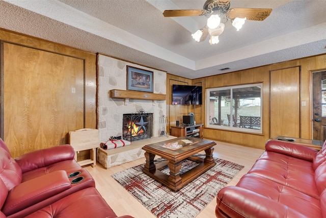 living room with a fireplace, wood finished floors, wood walls, and a textured ceiling