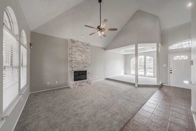 unfurnished living room featuring baseboards, carpet floors, high vaulted ceiling, a fireplace, and ceiling fan