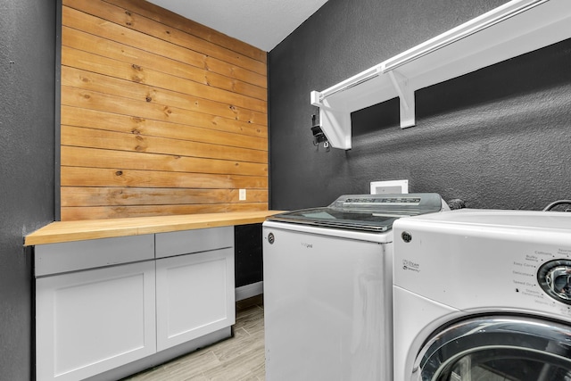 clothes washing area featuring laundry area, light wood-style flooring, separate washer and dryer, and a textured wall