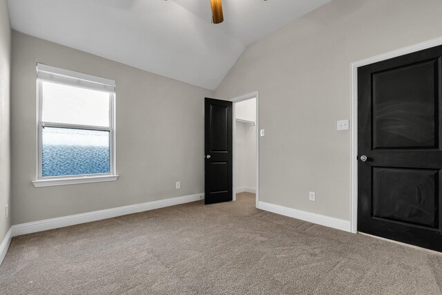 unfurnished bedroom with baseboards, vaulted ceiling, a spacious closet, a closet, and carpet flooring