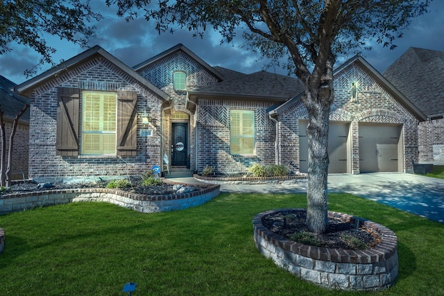 french country style house featuring driveway, a front lawn, roof with shingles, an attached garage, and brick siding