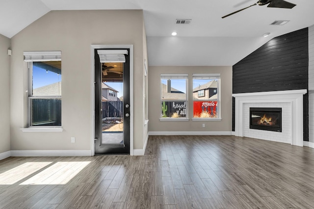 unfurnished living room with visible vents, a ceiling fan, wood finished floors, a fireplace, and vaulted ceiling