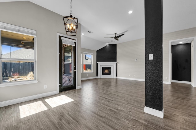 unfurnished living room featuring visible vents, ceiling fan with notable chandelier, wood finished floors, a fireplace, and vaulted ceiling