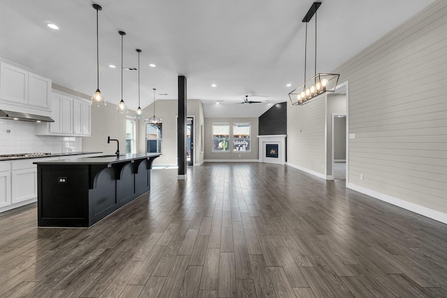 kitchen featuring a lit fireplace, cooktop, dark countertops, open floor plan, and backsplash